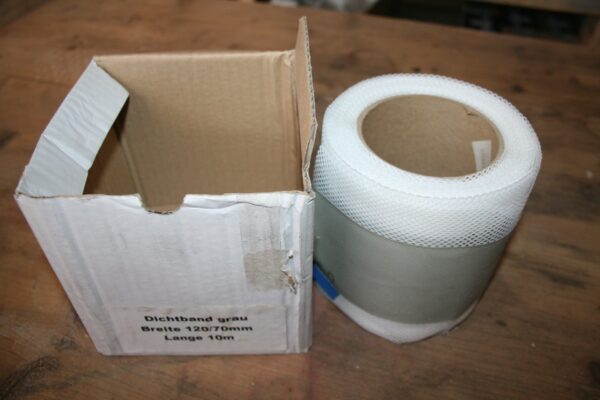 Rouleau neuf de bande d'étanchéité grise à bords en résille blanche, posé à côté de son carton d'origine marqué Dichtband grau, largeur 120/70 mm, longueur 10 m.