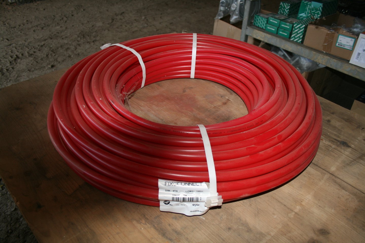 Couronne de tube PER nu rouge FixOConnect Ø16, 100 m, posée sur un établi en bois