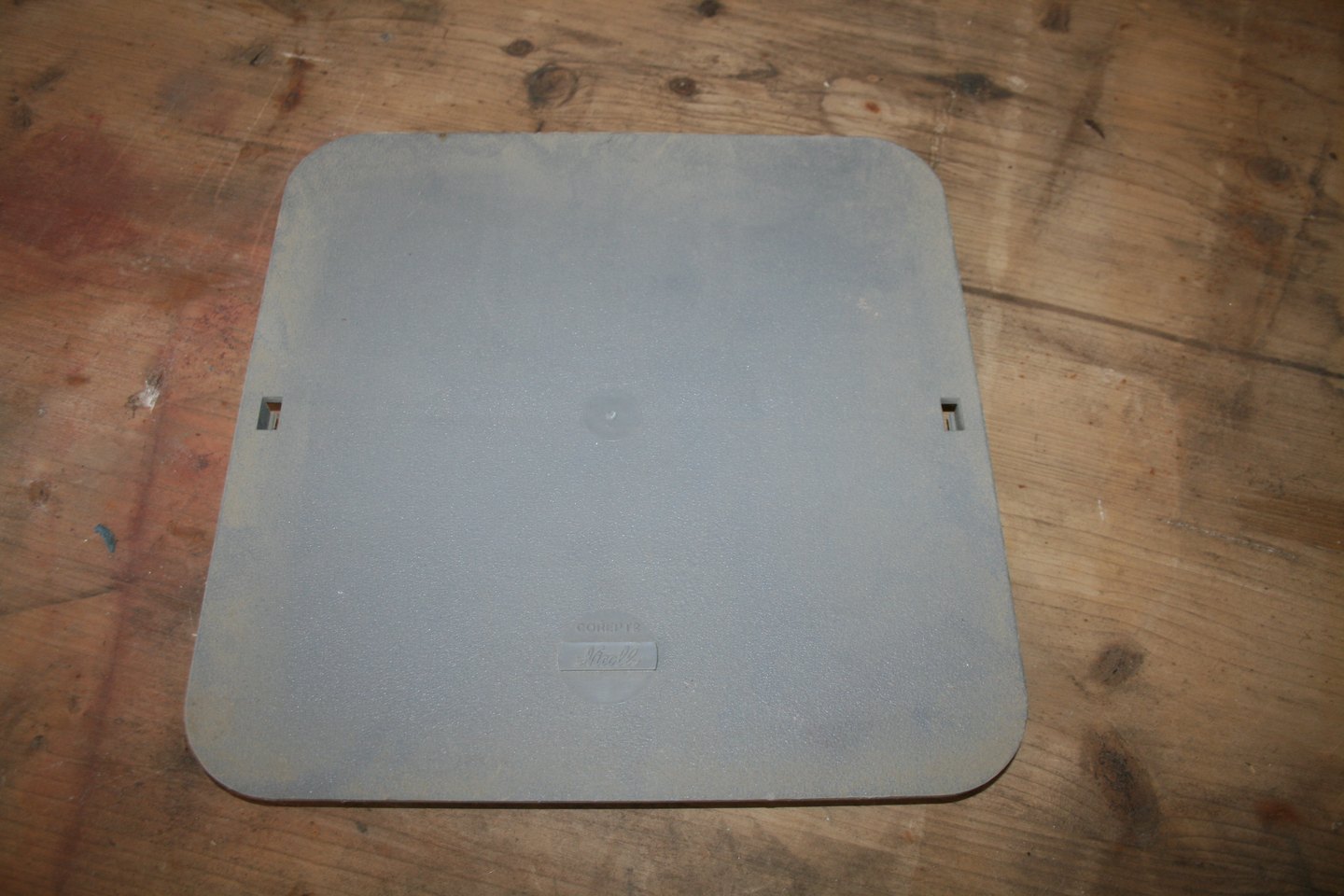 Couvercle carré en PVC gris-bleu Nicoll, logo moulé, posé sur un plancher en bois