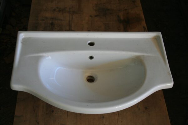 Lavabo à suspendre en céramique blanche vu de dessus, cuve ovale et un trou de robinetterie, posé sur un établi en bois