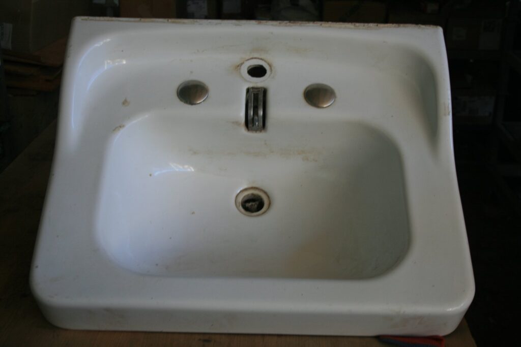 Lavabo rétro en céramique blanche vu de dessus, posé sur un établi, avec trois trous de robinetterie dont une tirette centrale de bonde