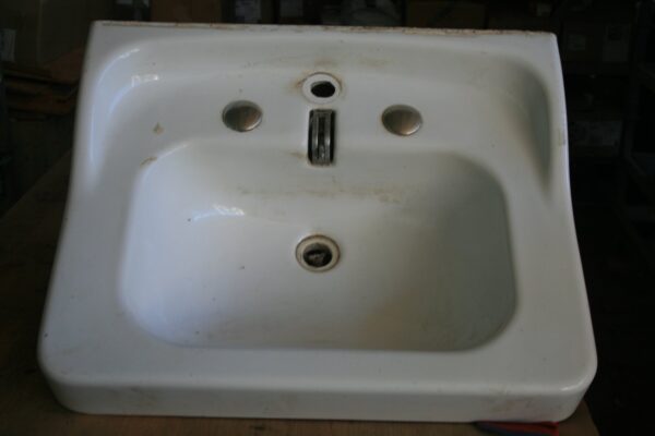 Lavabo rétro en céramique blanche vu de dessus, posé sur un établi, avec trois trous de robinetterie dont une tirette centrale de bonde