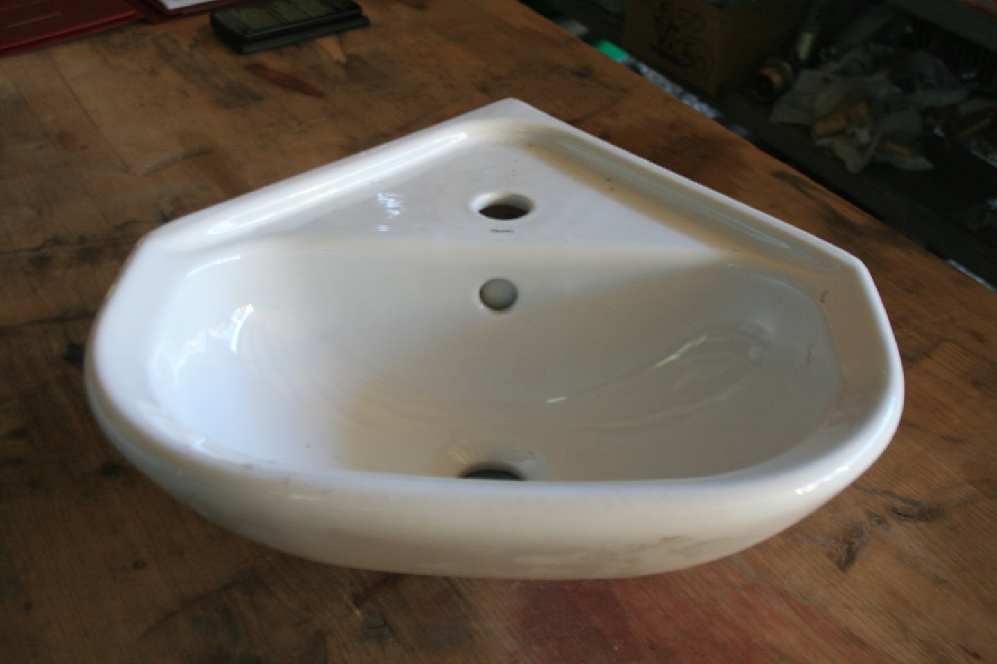 Lave-mains d'angle en céramique blanche posé sur un établi en bois, trou de robinet sur la tablette et bonde à l'avant de la cuve