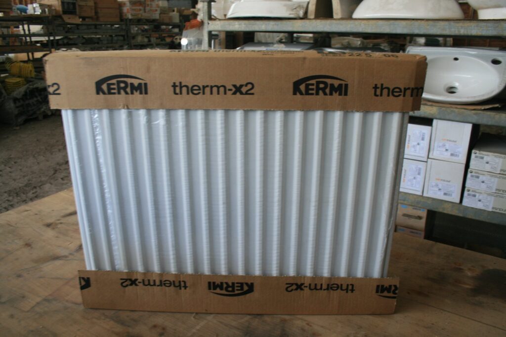 Radiateur panneau acier Kermi therm-X2 dans son emballage d'origine (cornières carton et film), étiquette « 22 5 06 », posé sur un établi