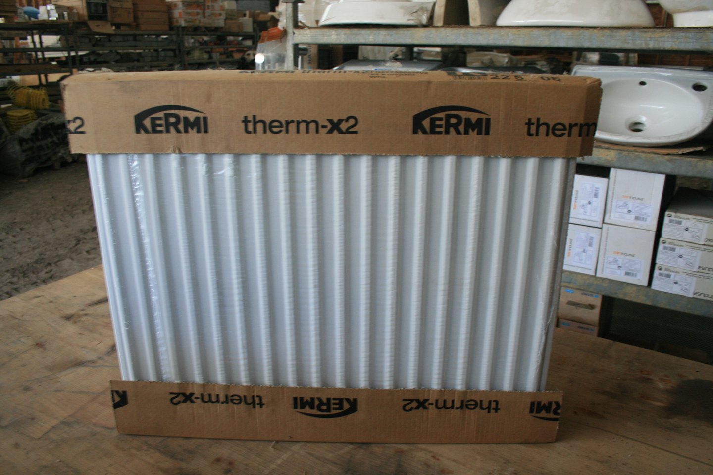 Radiateur panneau acier Kermi therm-X2 dans son emballage d'origine (cornières carton et film), étiquette « 22 5 06 », posé sur un établi