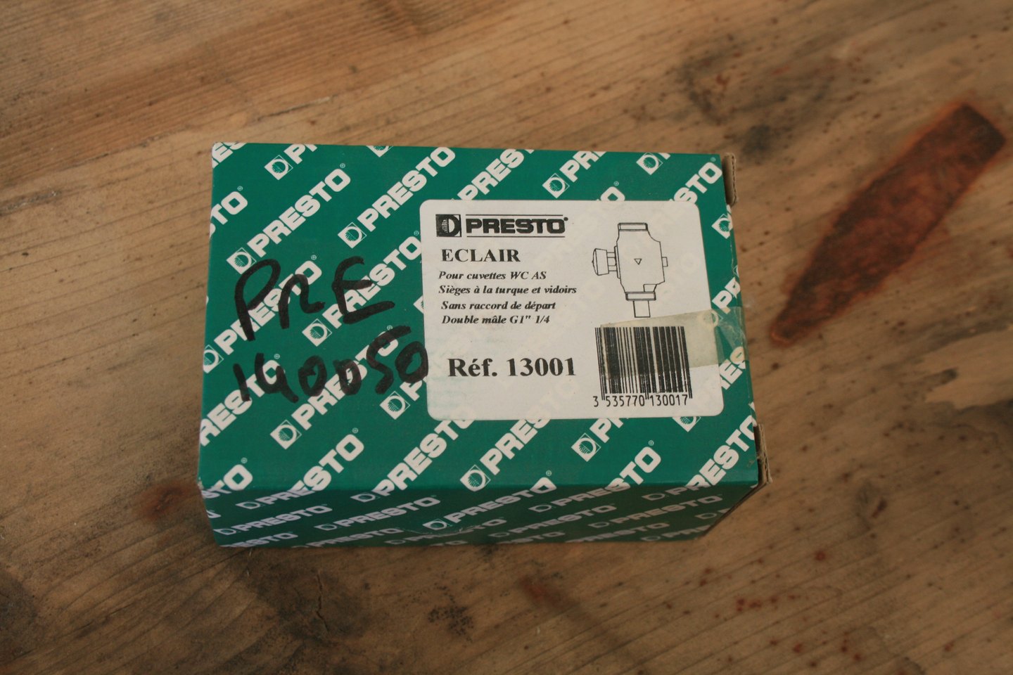 Carton neuf du robinet de chasse temporisé Presto Eclair pour WC à la turque, référence 13001, posé sur un plan en bois.