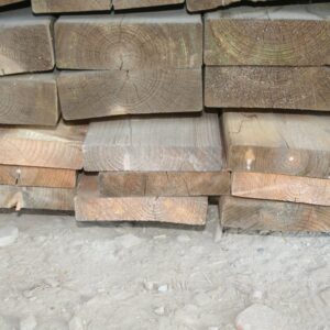 Pile de pièces de bois de charpente empilées, têtes de section visibles avec fentes de retrait et teintes grisées ou orangées