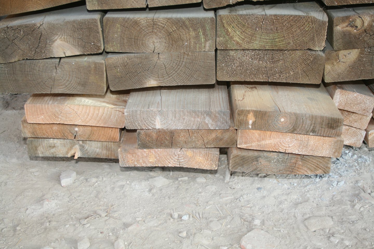 Pile de pièces de bois de charpente empilées, têtes de section visibles avec fentes de retrait et teintes grisées ou orangées