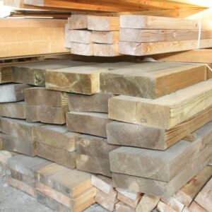 Pile de madriers plats en bois résineux de teinte brun-vert, cerclés de sangles blanches, stockés dans le hangar de La Bricothèque