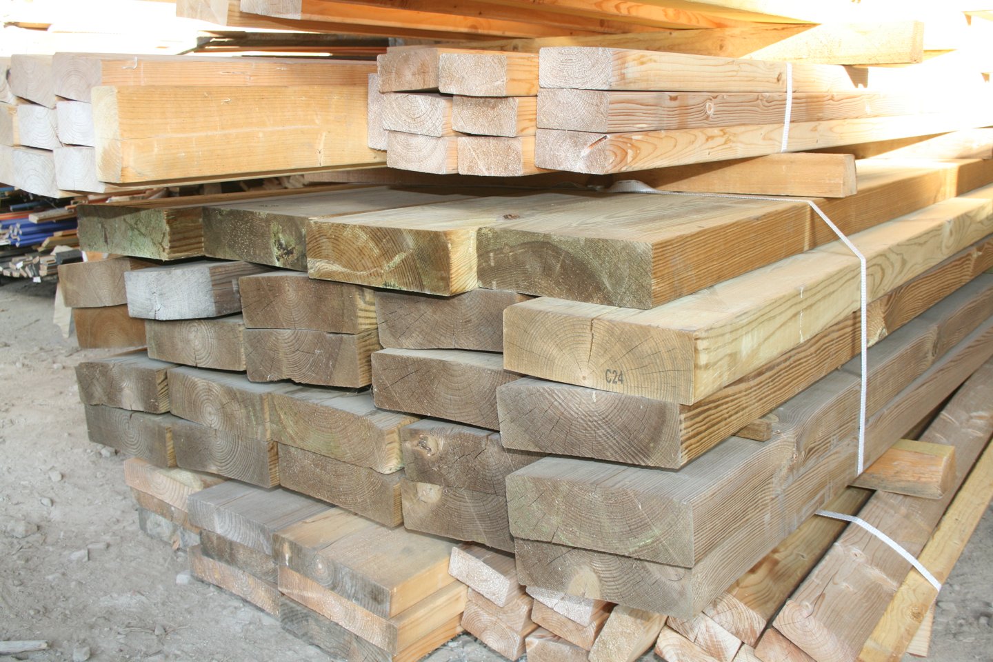 Pile de madriers plats en bois résineux de teinte brun-vert, cerclés de sangles blanches, stockés dans le hangar de La Bricothèque