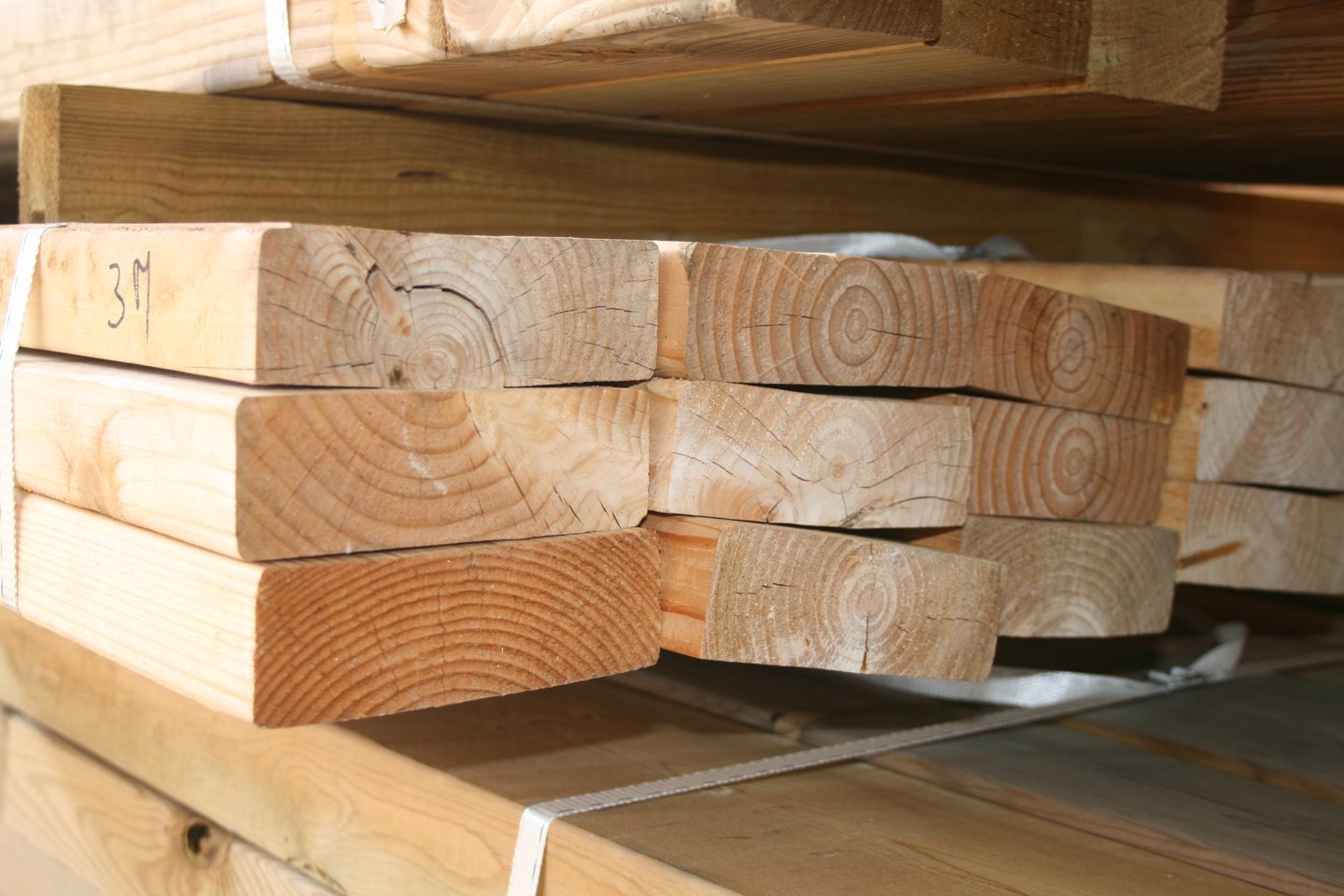 Paquets de pièces de bois de structure empilées et cerclées, avec l'inscription 3M au marqueur sur la pièce du dessus