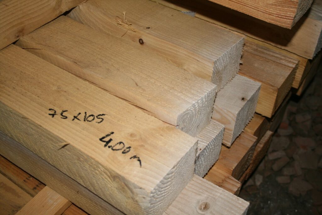 Pile de chevrons en bois brut avec la section 75x105 et la longueur 4,00 m écrites au marqueur noir sur la pièce du premier plan
