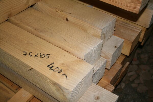 Pile de chevrons en bois brut avec la section 75x105 et la longueur 4,00 m écrites au marqueur noir sur la pièce du premier plan