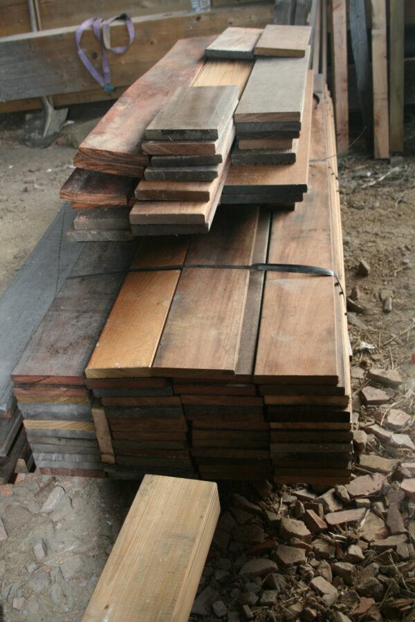 Pile de lames de terrasse en bois exotique cerclées, teintes brun-rouge et grisées, dans un hangar
