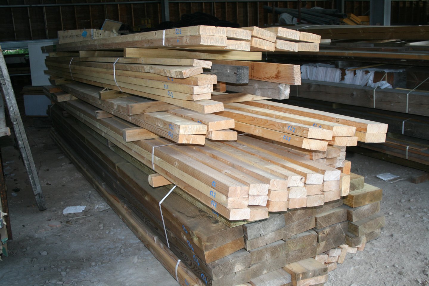 Vue générale du stock de bois d'ossature et de charpente de La Bricothèque, pièces empilées sous hangar